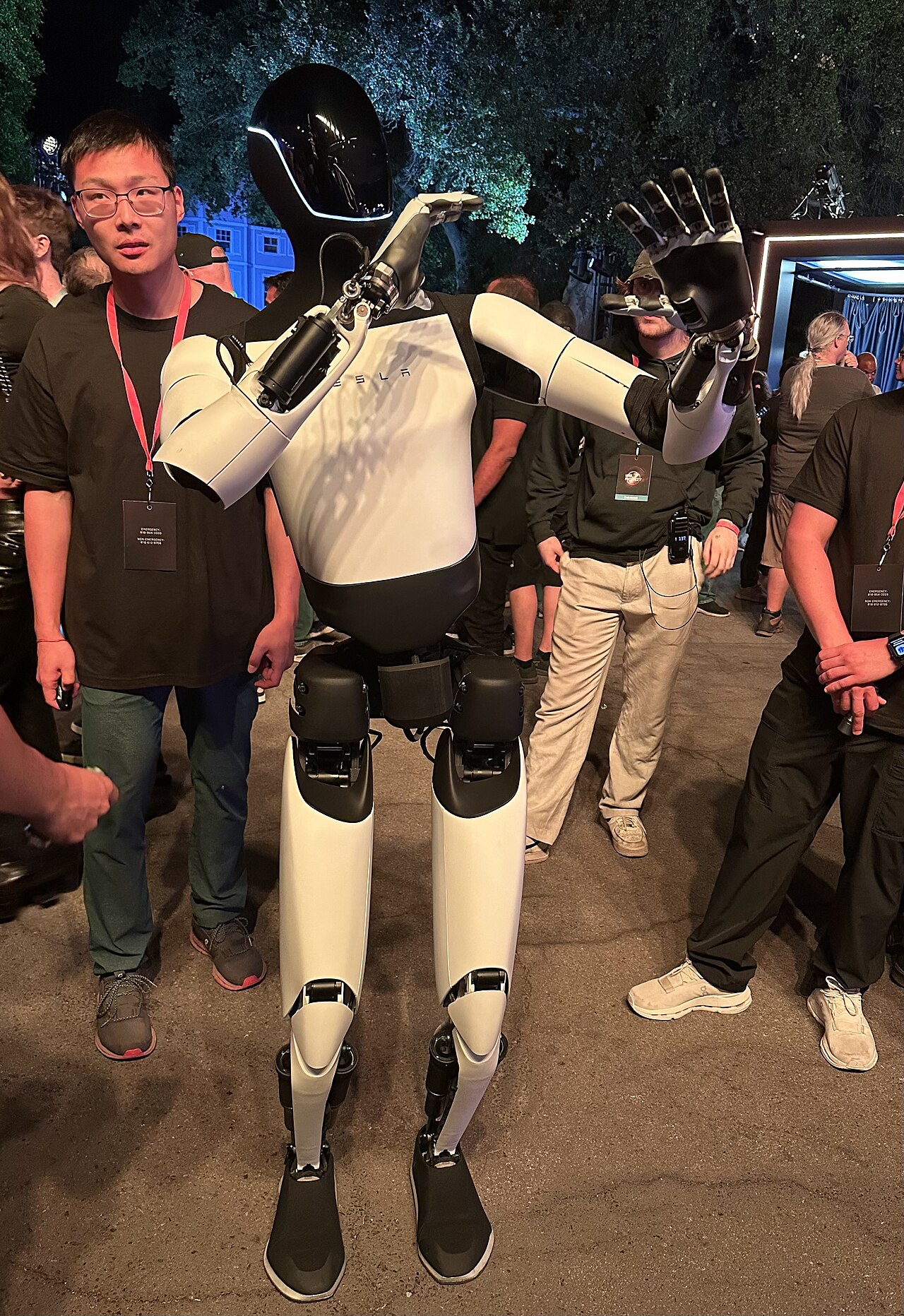 A Tesla Optimus humanoid robot standing among a crowd at an evening event
